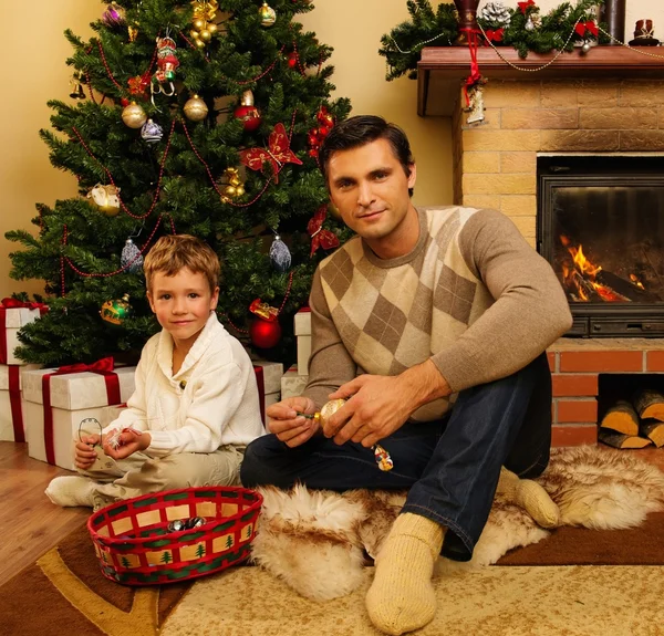 Padre joven con su hijo cerca de la chimenea en el interior de la casa decorada de Navidad — Foto de Stock