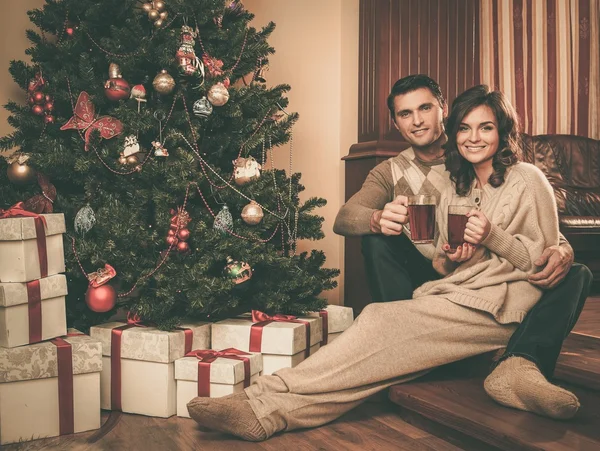 Paar mit Tassen Heißgetränk in der Nähe des Weihnachtsbaums — Stockfoto