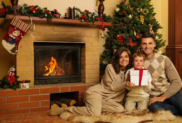Familia cerca de la chimenea en Navidad decorado interior de la casa con caja de regalo — Foto de Stock