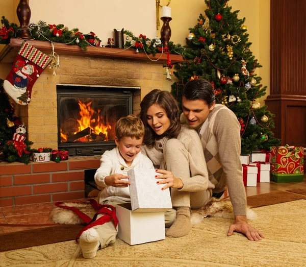 Семья возле камина в украшенном рождественским интерьером доме с подарочной коробкой — стоковое фото