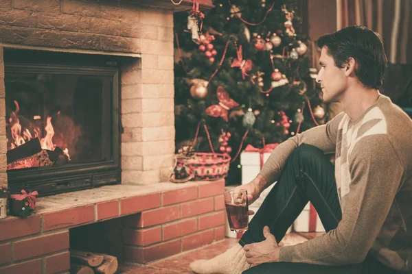 Hombre con taza de bebida caliente cerca de la chimenea en la casa decorada de Navidad —  Fotos de Stock