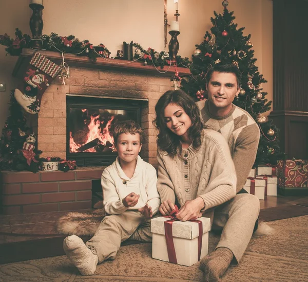 Família perto de lareira no interior da casa decorada de Natal com caixa de presente — Fotografia de Stock