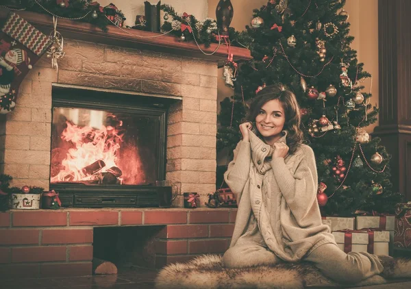 Mujer joven cerca de la chimenea en el interior de la casa decorada de Navidad —  Fotos de Stock