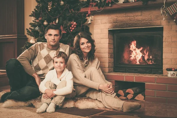 Семья возле камина в украшенном рождественским интерьером доме с подарочной коробкой — стоковое фото