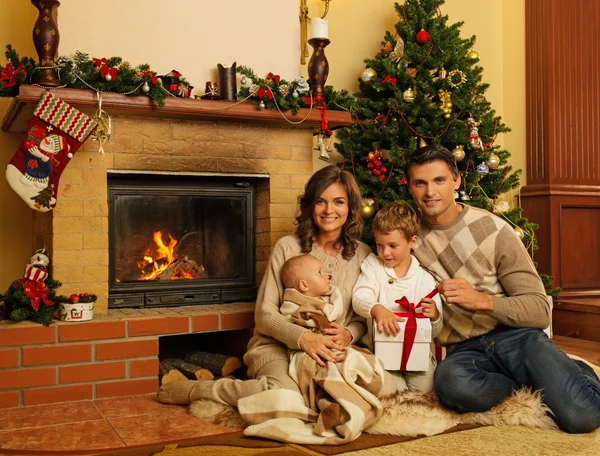 Familia cerca de la chimenea en Navidad decorado interior de la casa con caja de regalo — Foto de Stock