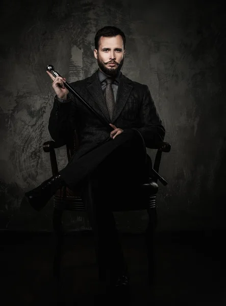 Handsome well-dressed man with walking stick sitting in leather chair — Stock Photo, Image