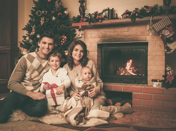 Familia cerca de la chimenea en Navidad decorado interior de la casa con caja de regalo — Foto de Stock