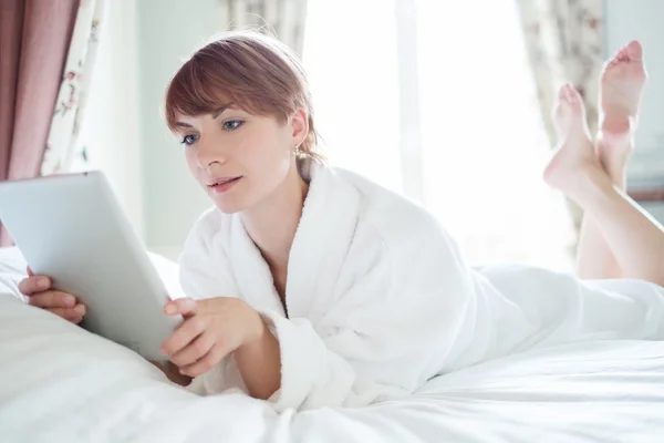 Piękna kobieta w szlafrok, leżąc na łóżku z komputera typu tablet — Zdjęcie stockowe