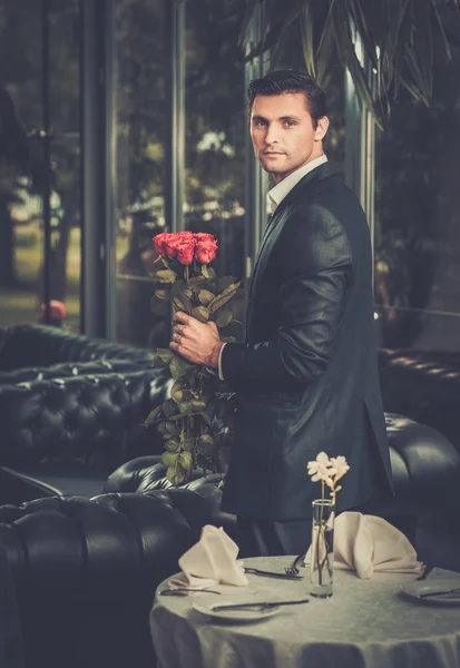 Bonito homem com um monte de rosas vermelhas esperando sua senhora no restaurante — Fotografia de Stock