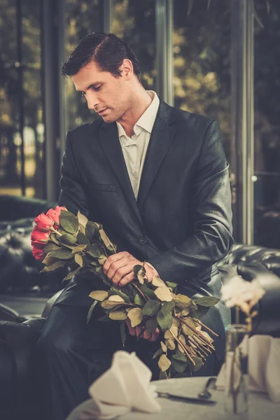 Bonito homem com um monte de rosas vermelhas esperando sua senhora no restaurante — Fotografia de Stock