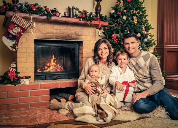 Familia cerca de la chimenea en Navidad decorado interior de la casa con caja de regalo — Foto de Stock