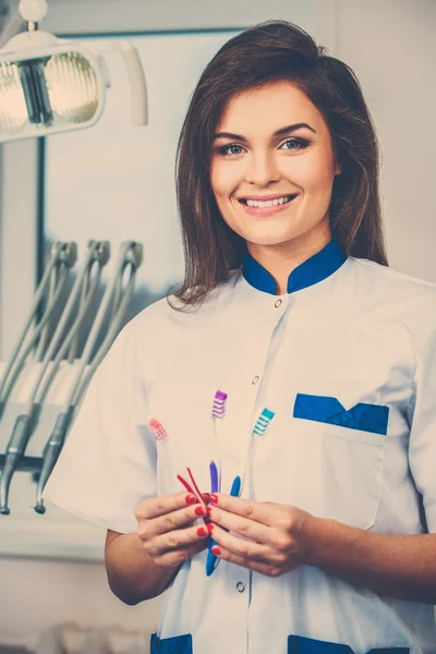 Jovem linda morena dentista feminina com três escovas de dentes na cirurgia do dentista — Fotografia de Stock