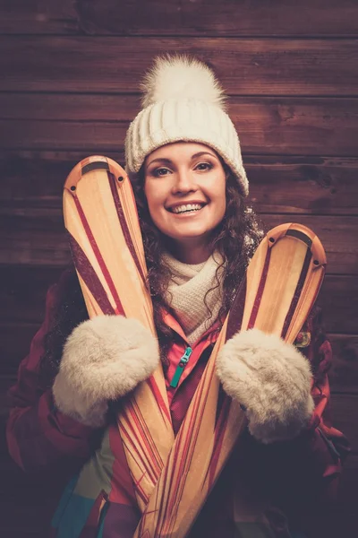 Mujer sonriente con esquís de pie contra la pared de la casa de madera —  Fotos de Stock