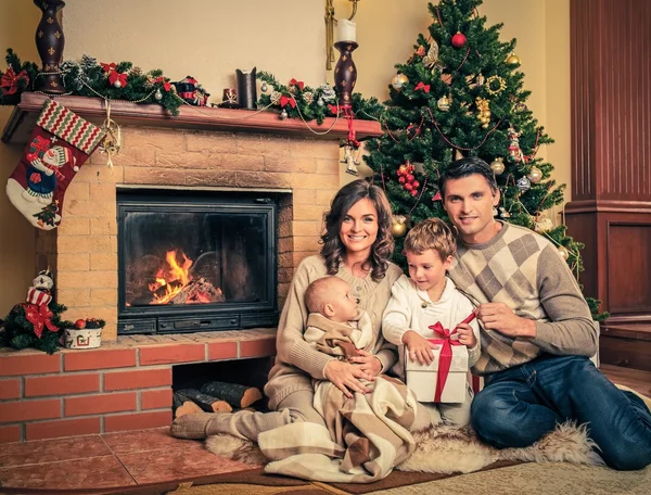 Família perto de lareira no interior da casa decorada de Natal com caixa de presente — Fotografia de Stock