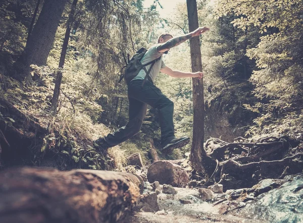 Человек-турист, перепрыгивающий через реку в горном лесу — стоковое фото