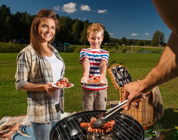 Jonge gezin voorbereiding worstjes op een grill buiten — Stockfoto