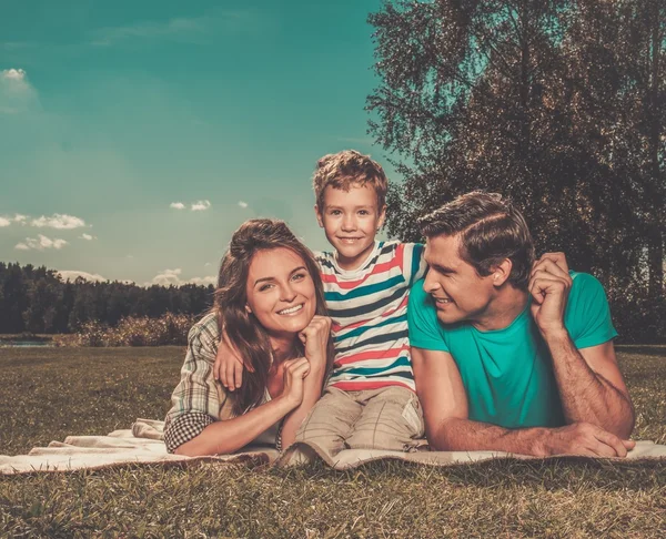 Jonge gezin met hun kind liggend op een deken in de buitenlucht — Stockfoto