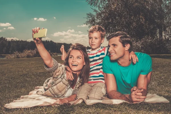 Família jovem com seu filho fazendo selfie em um cobertor ao ar livre — Fotografia de Stock