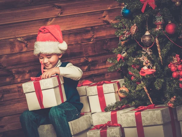 Little boy with gift box under christmas tree in wooden house interior — Stock Photo, Image