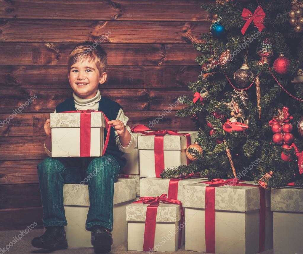Little boy with gift box under christmas tree in wooden house interior