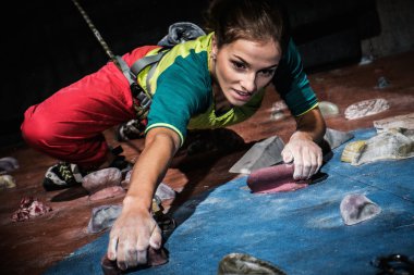 Young woman practicing rock-climbing on a rock wall indoors clipart