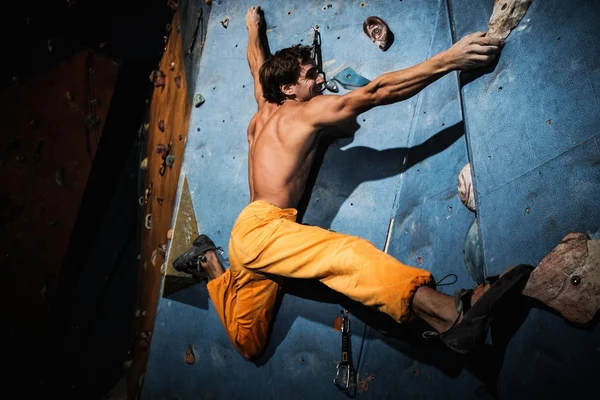 Homem musculoso praticando escalada em uma parede de rocha dentro de casa — Fotografia de Stock