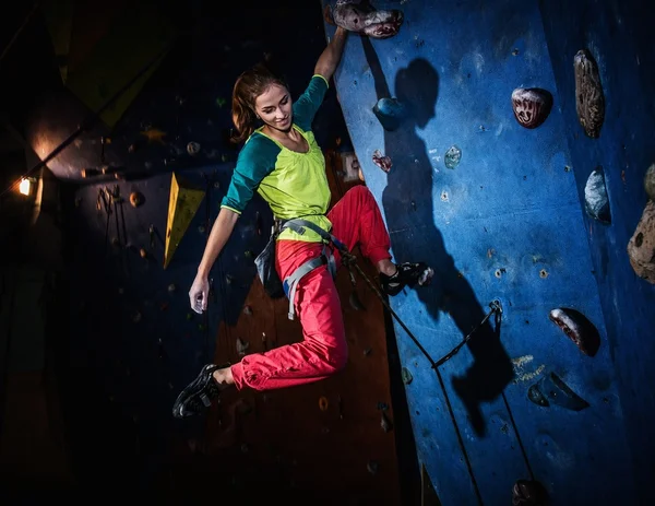 Young woman practicing rock-climbing on a rock wall indoors — Stock Photo, Image