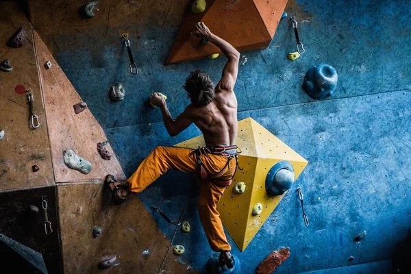 Muscular man practicing rock-climbing on a rock wall indoors — Stock Photo, Image