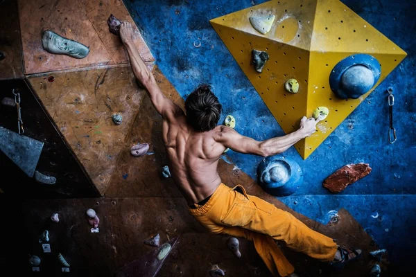 Homem musculoso praticando escalada em uma parede de rocha dentro de casa — Fotografia de Stock