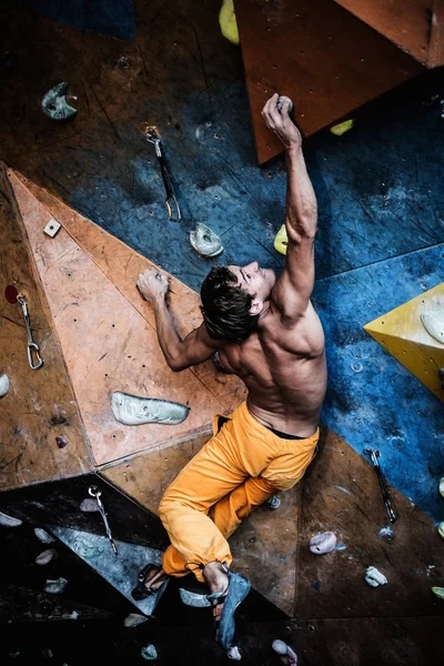 Homem musculoso praticando escalada em uma parede de rocha dentro de casa — Fotografia de Stock