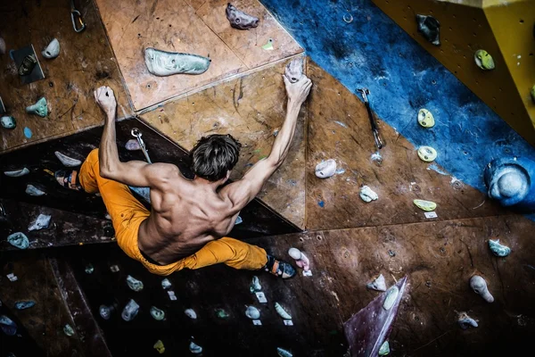 Hombre musculoso practicando escalada en roca en una pared de roca en el interior —  Fotos de Stock