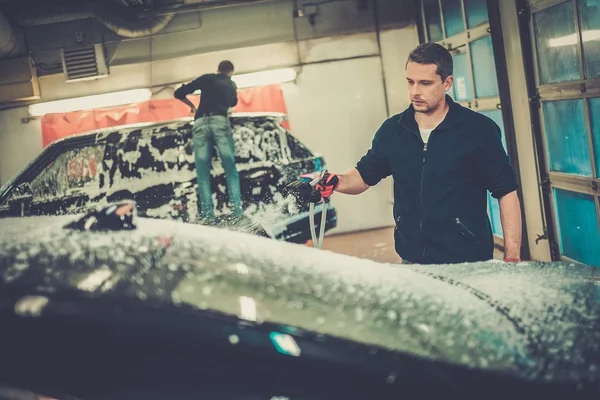 Homem trabalhador lavar carro de luxo em uma lavagem de carro — Fotografia de Stock