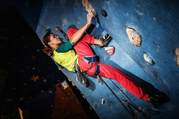 Mujer joven practicando escalada en roca en una pared de roca en el interior —  Fotos de Stock