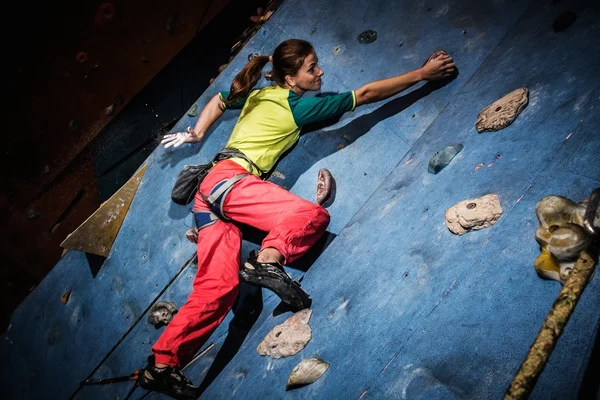 Mujer joven practicando escalada en roca en una pared de roca en el interior —  Fotos de Stock