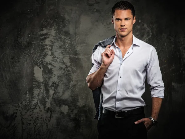 Handsome man in shirt against grunge wall holding jacket over shoulder — Stock Photo, Image