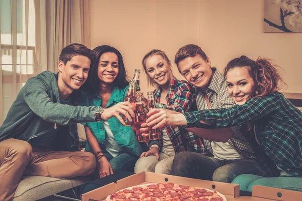 群年轻多族裔朋友比萨饼和饮料庆祝在家庭内部的瓶子 — 图库照片