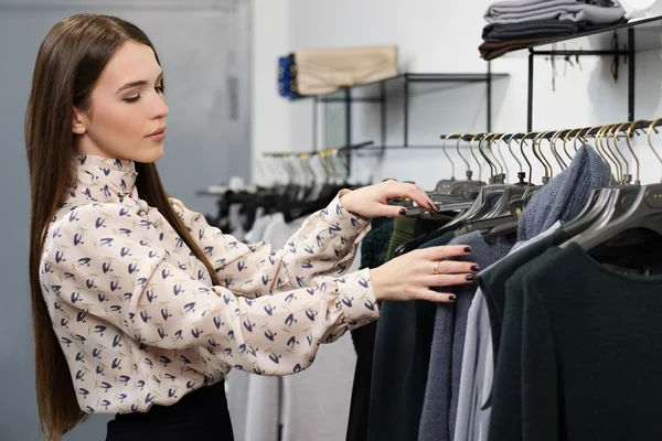 Mujer eligiendo ropa en un estante en una sala de exposición — Foto de Stock