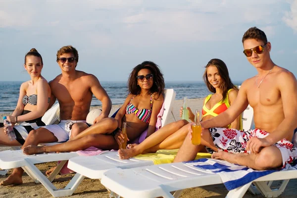 Grupo de amigos multiétnicos tomando el sol en una tumbona en una playa —  Fotos de Stock