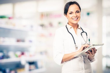 Positive brunette doctor woman in drug store with tablet pc clipart