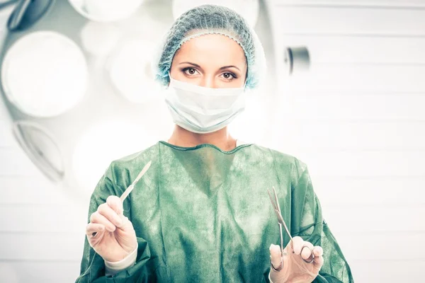 Jovem médica com bisturi e tesoura na sala de cirurgia — Fotografia de Stock