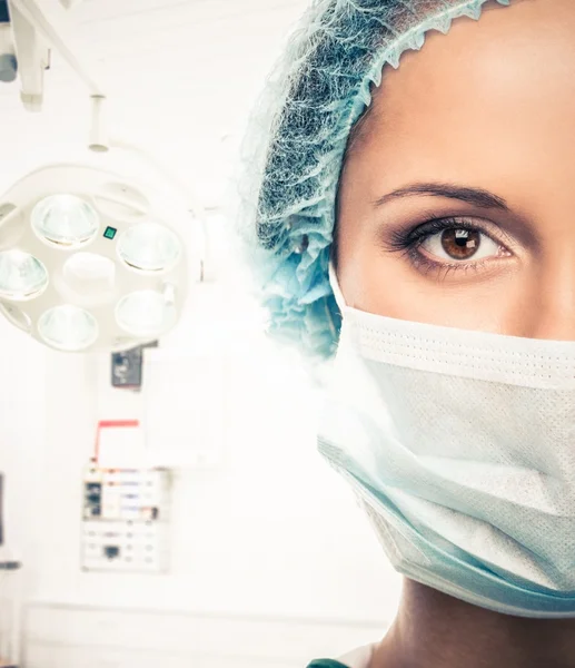 Mladá žena doktor v čepici a obličejovou masku v interiéru místnosti chirurgie — Stock fotografie