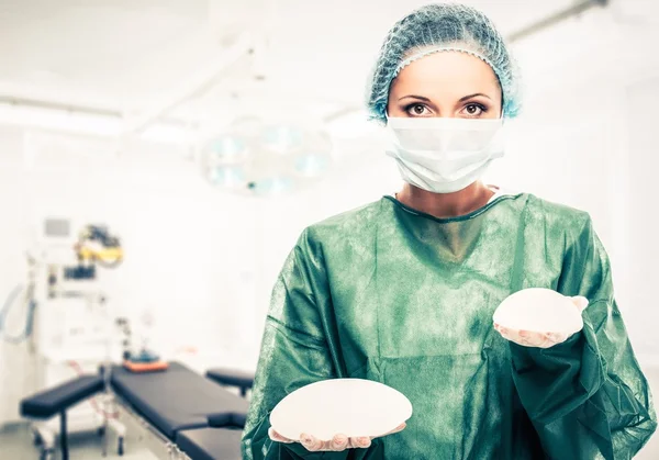 Пластическая хирург женщина держит разного размера силиконовые грудные имплантаты в интерьере операционного зала — стоковое фото