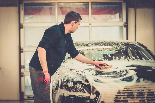 Hombre trabajador lavando coche de lujo con esponja en un lavado de coches —  Fotos de Stock