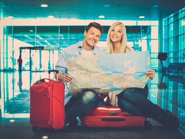 Jong koppel met kaart zittend op koffers in luchthaven — Stockfoto