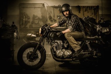 Rider and his vintage style cafe-racer motorcycle in customs garage  clipart