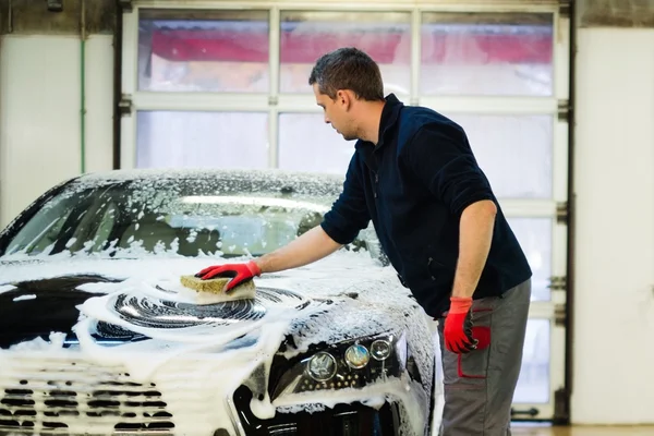 Hombre trabajador lavando coche de lujo con esponja en un lavado de coches — Foto de Stock