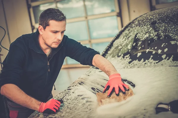 Hombre trabajador lavando coche de lujo con esponja en un lavado de coches — Foto de Stock