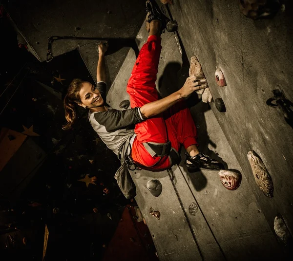 Mujer joven practicando escalada en roca en una pared de roca en el interior —  Fotos de Stock