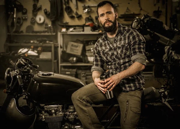 Rider and his vintage style cafe-racer motorcycle in customs garage — Stock Photo, Image