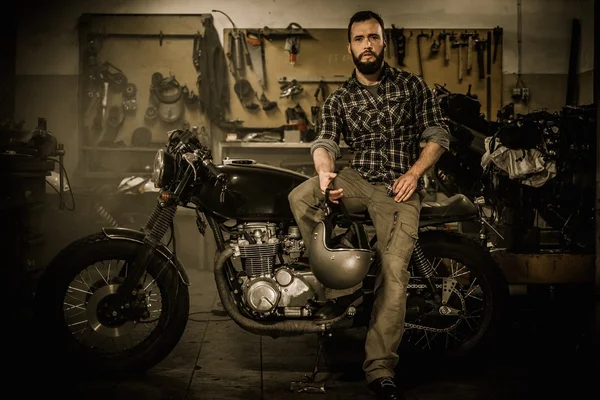 Гонщик и его мотоцикл в винтажном стиле в таможенном гараже — стоковое фото